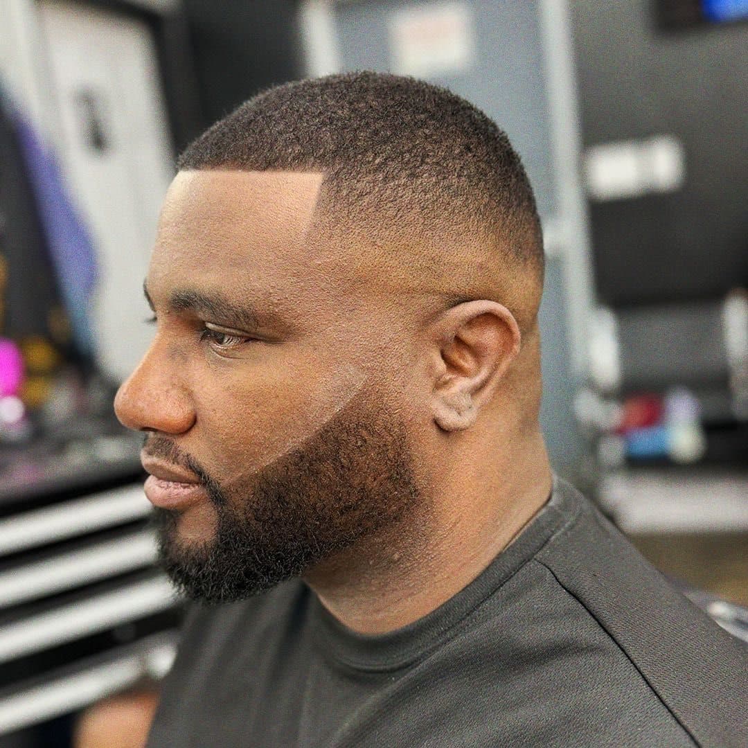 Un taper fade fundido con una barba completa, visto de perfil