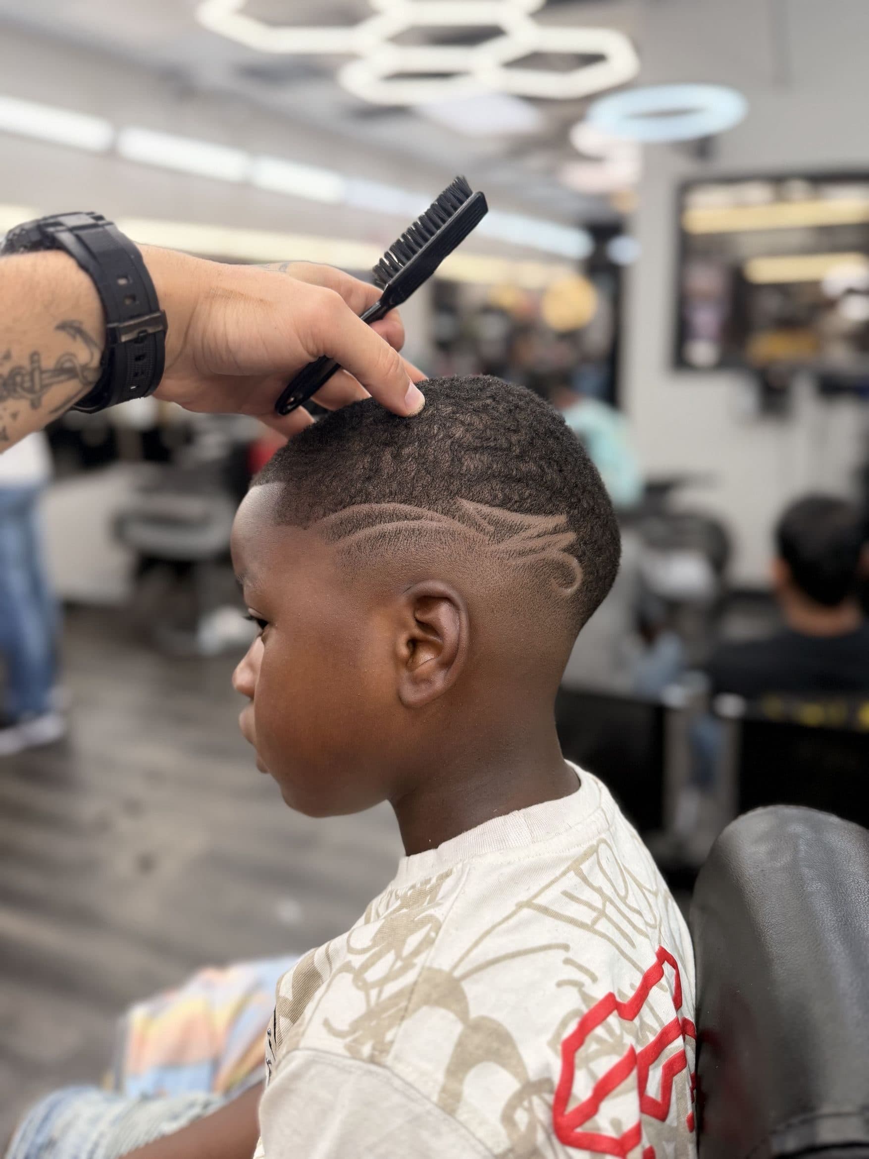 Un diseño a mano alzada en el fade de un cliente joven, con la barbería de fondo