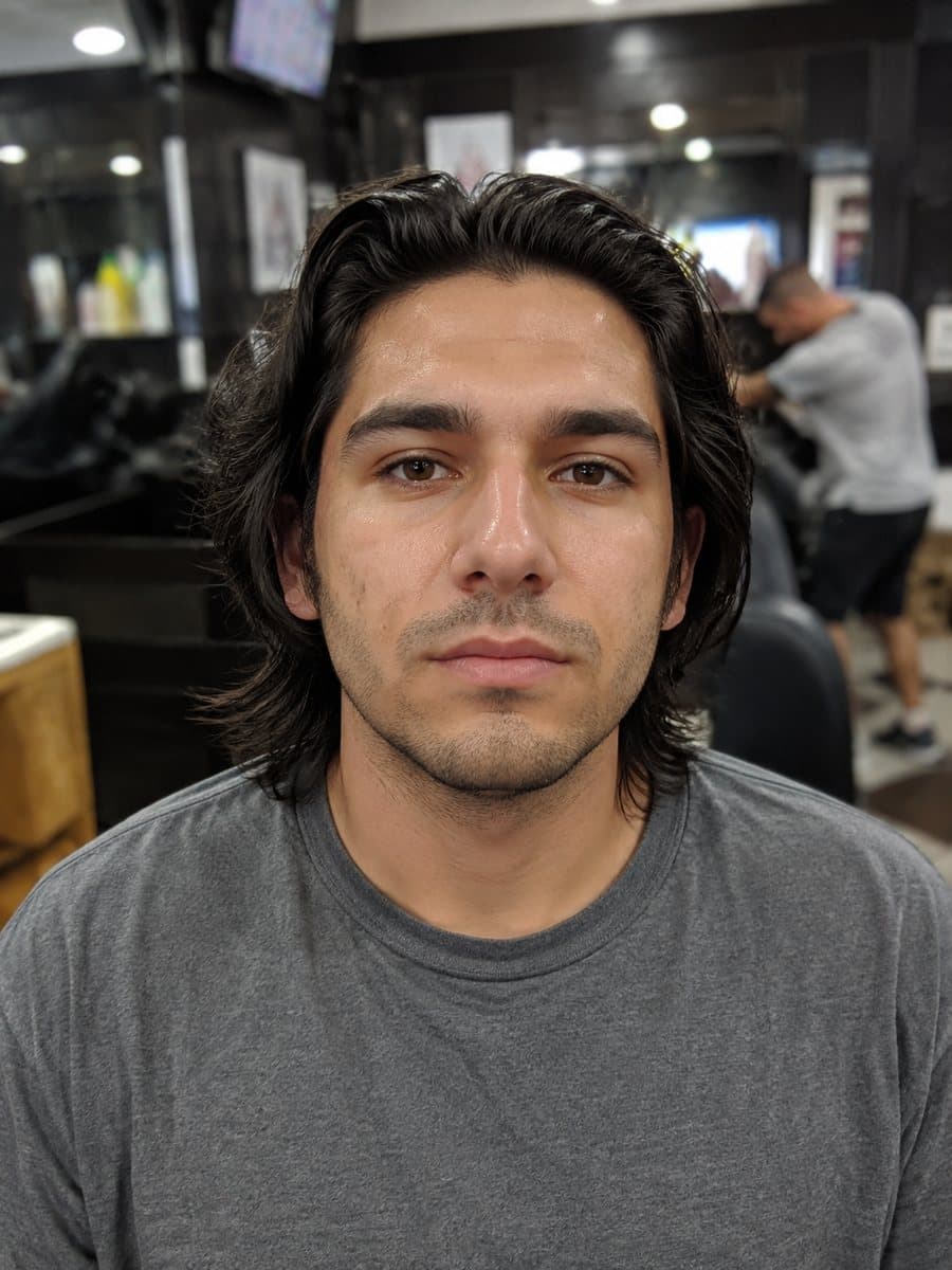 Un hombre con cabello oscuro largo hasta la mandíbula, fotografiado de frente en una barbería